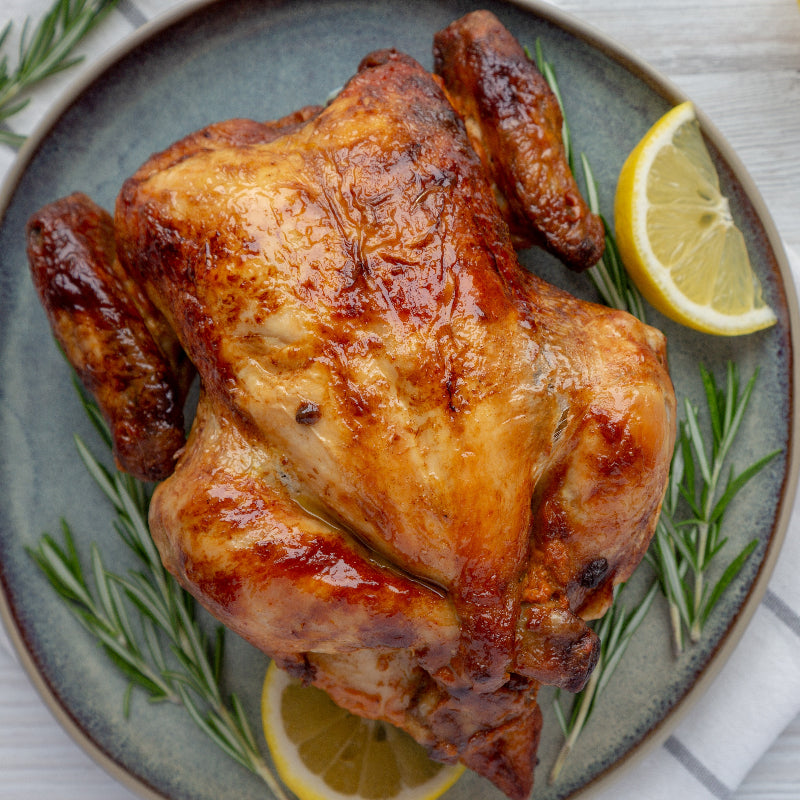 Roasted chicken on a plate with lemon slices and rosemary on a light wooden background